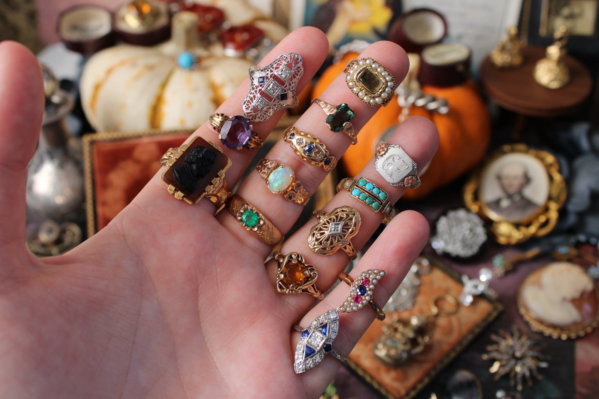Hand wearing multiple rings with a variety of gemstones against a decorative background