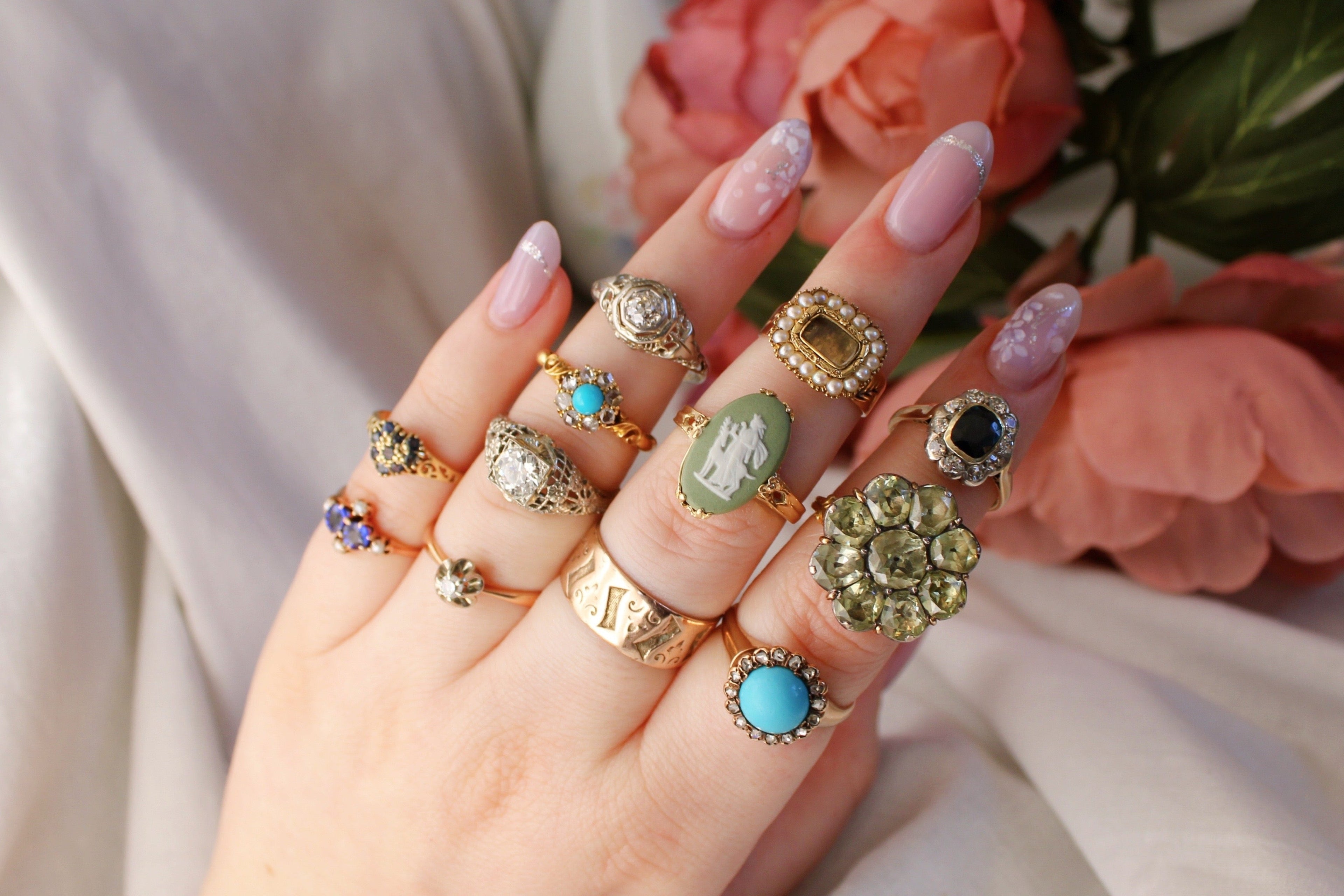 Hand wearing multiple rings with colorful gemstones against a soft floral background