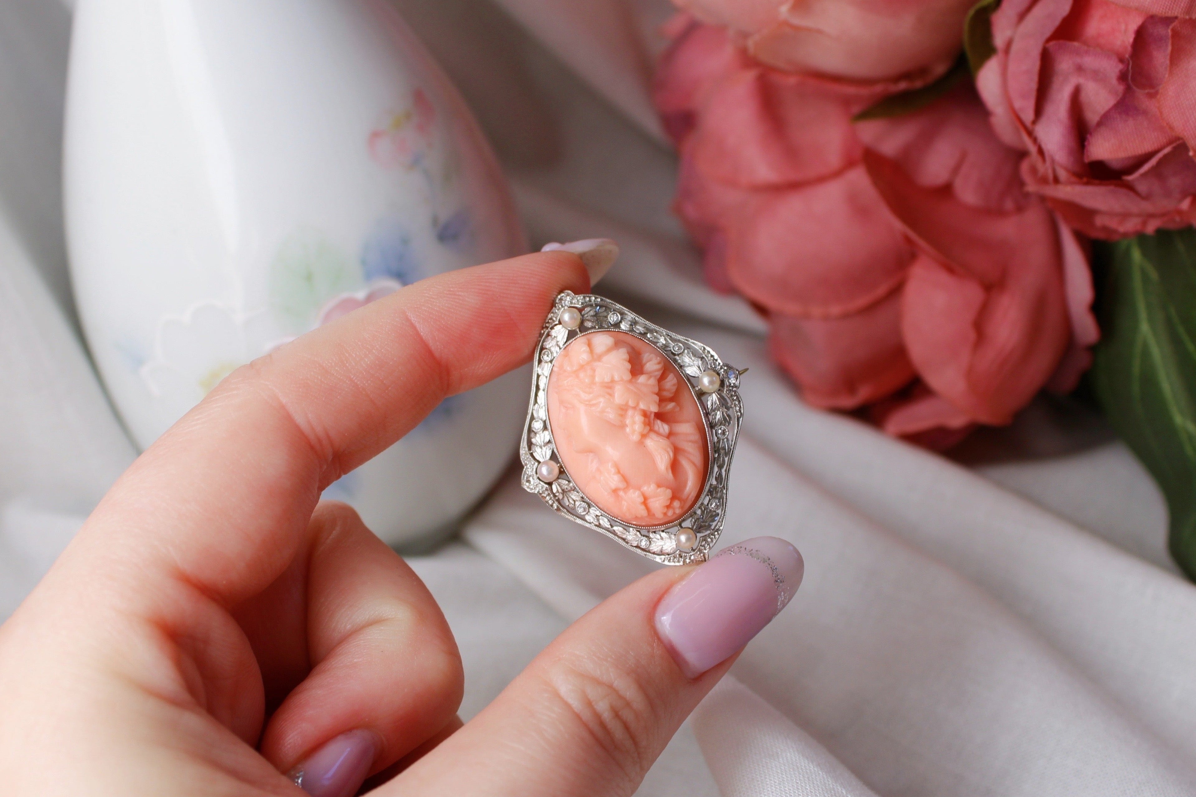 Hand holding a pink brooch with floral background