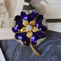 Gold and purple flower-shaped brooch with gemstones on a textured surface