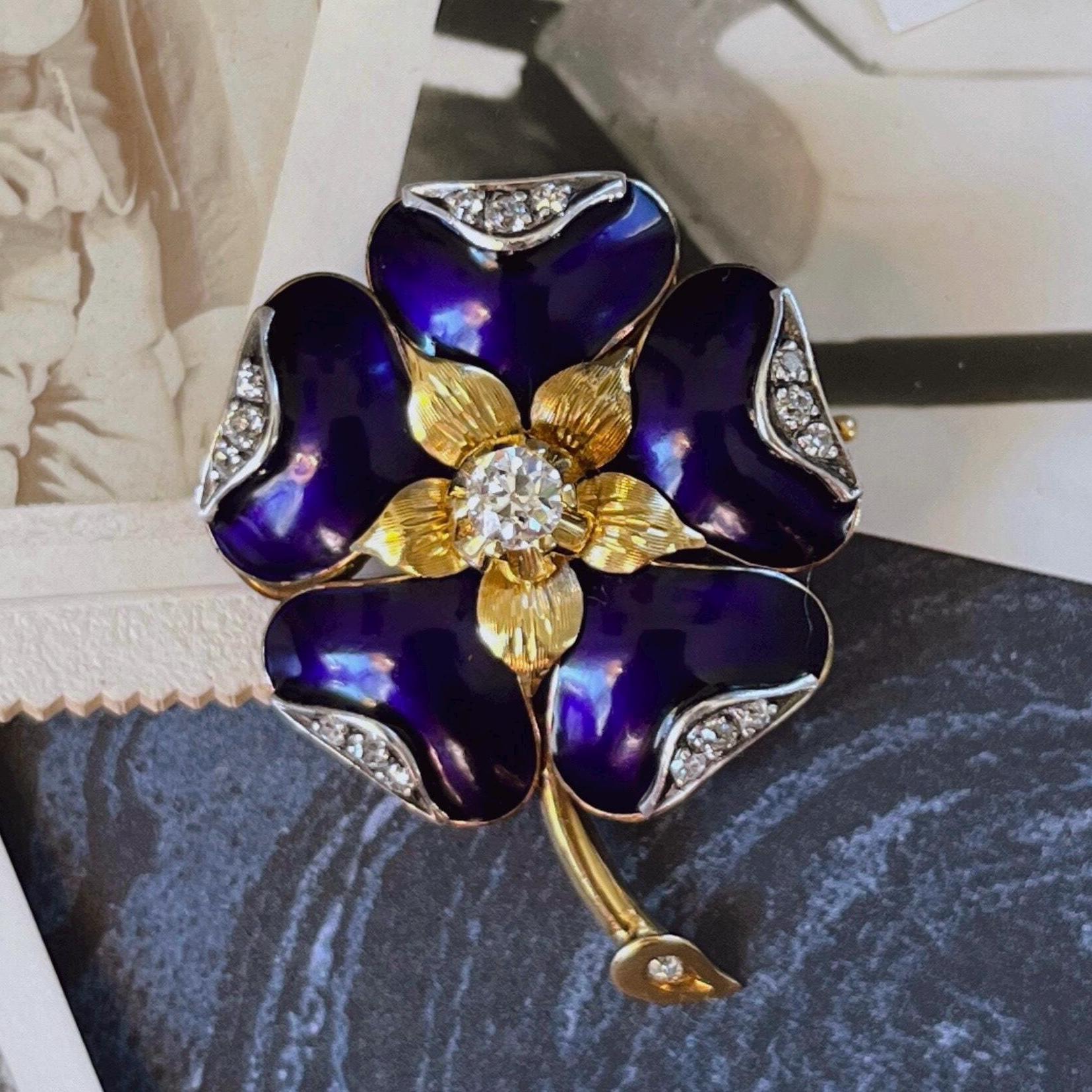Gold and purple flower-shaped brooch with gemstones on a textured surface